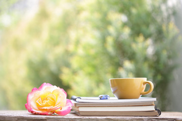 Yellow cup with yellow rose and notebooks at outdoor