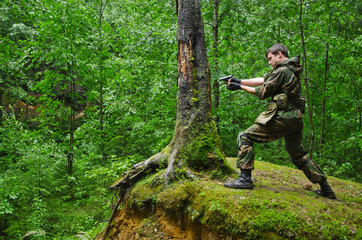 Fototapeta premium soldier aims and shoots standing in a fighting stand on a hill in the forest