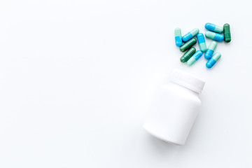 Color pills spilling out of a pill bottle on white background top view copy space