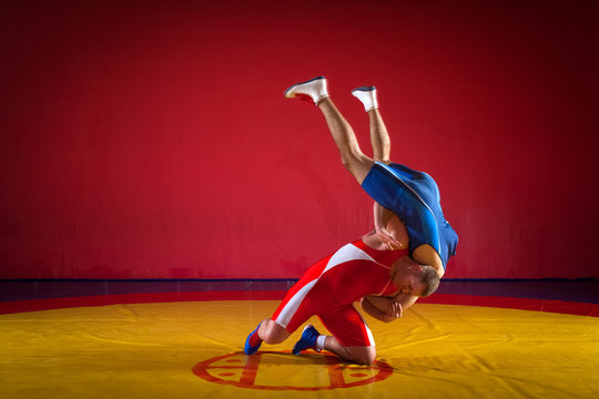 Two strong wrestlers in blue and red wrestling tights  making a hip throw  on a yellow wrestling carpet in the gym. Young man doing grapple.