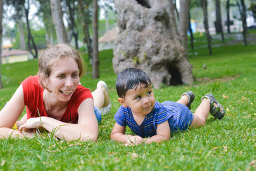 Naklejka na ściany i meble Happy biracial family in the summer park - caucasian mother with her latin son laying on the grass.