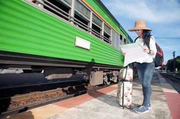Pretty Asian traveler backpacker female looking map and waiting train at railway station in Thailand.