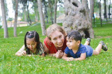 Fototapeta premium Happy biracial family in the summer park - caucasian mother with her latin children laying on the grass.