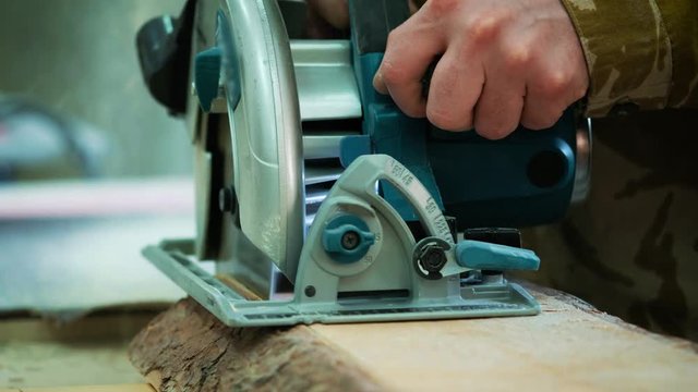 Cutting wooden floor by electric saw. The carpenter saws a log or board
