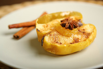 On the plate is a baked apple, near cinnamon, anise. Wicker substrate, composition. Close-up