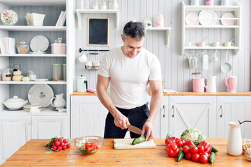 Portrait of handsome smiling man at kitchen. cooking and home concept - close up of male hand chopping cucumber on cutting board with sharp knife