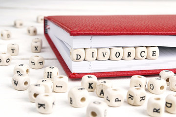 Word Divorce written in wooden blocks in red notebook on white wooden table.