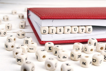 Word Dispute written in wooden blocks in red notebook on white wooden table.