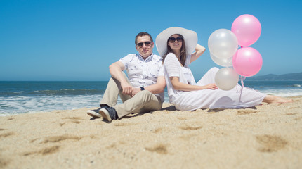 Fototapeta premium Young romantic couple with balloons sitting on the beach