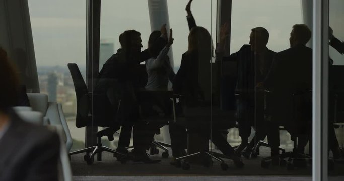 4k, Group of businesspeople high five together while standing in a modern boardroom. Slow motion.