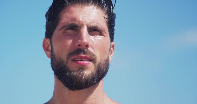 Portrait face serious attractive young man looking forward wearing a headset shining sun in her eyes on the beach at sea close up handsome headphones ocean outdoors music water casual enjoying relax