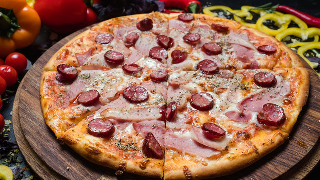 national italian cuisine. pizza with ham and prosciutto and pepperoni fresh vegetables in background