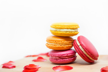 Sweet dessert and colourful french macaroons or macaron on wooden white background, Around with red rose petals in Valentine's Day theme.