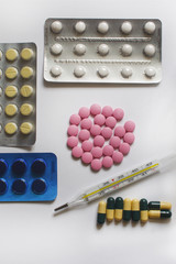 Pink, yellow and white pills, medicine and thermometer on white background