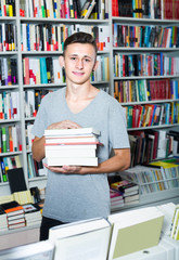 teenage boy with book pile in shop.