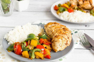 Baked chicken breast with colorful grilled bell peppers and rice served for two on grey plate.
