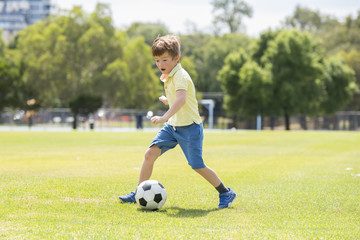 Fototapeta premium little kid 7 or 8 years old enjoying happy playing football soccer at grass city park field running and kicking the ball excited in childhood sport passion