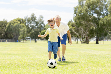 young happy father and excited little 7 or 8 years old son playing together soccer football on city park garden running on grass kicking the ball