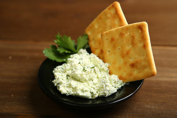On a dark plate a portion of cottage cheese with greens is decorated with parsley. Low-calorie cookies. Wooden table, dark background. One light source. A healthy diet for those who control their body