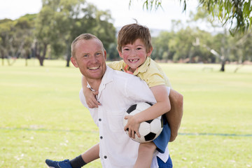 young happy father carrying on his back excited 7 or 8 years old son playing together soccer football on city park garden posing sweet and loving