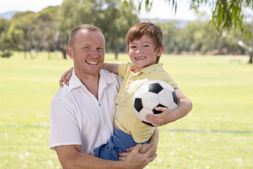 young happy father carrying on his back excited 7 or 8 years old son playing together soccer football on city park garden posing sweet and loving