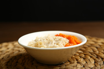 Low-calorie porridge for a healthy diet and lifestyle. Barley with honey and bits of orange pumpkin in a deep white plate. Dark background, wooden table and wicker stand