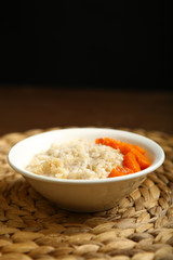 Low-calorie porridge for a healthy diet and lifestyle. Barley with honey and bits of orange pumpkin in a deep white plate. Dark background, wooden table and wicker stand