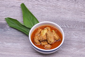 Top view of Thai Red curry with pork ribs in white bowl on Galangal leaf and wooden background. , Thai Southern style. © chattrakarn