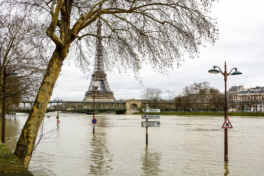 The swollen Seine during the winter flooding episode of January 2018, with half immersed road signs and street lights in the foreground and the Eiffel tower and Bir-Hakeim bridge in the background.
