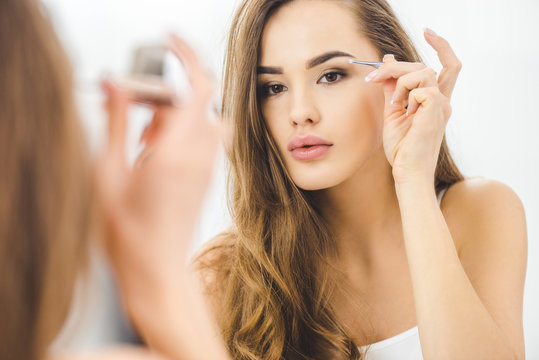 Young Woman Plucking Eyebrows With Tweezers