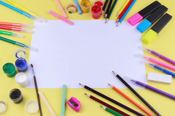 Fototapeta premium paper with colored crayons, brush, pencils and paints on yellow background. Top view . Flat lay image.Working desk table concept.