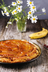 Traditional homemade banana caramel pie on vintage wooden table decorated a bouquet of chamomiles. Upside down banana cake. Selective focus 