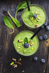 Smoothie with green spinach, pistachio on dark wooden board. Well being and weight loss concept.