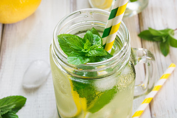 Summer refreshing detox cocktail. Water with lemon, mint and ice in mason jar on wooden board. Rustic style. Close up.