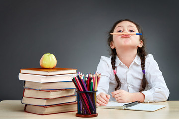 Playful cute little girl having fun while leaning on thick books on the grey background