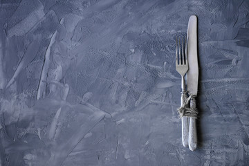 Vintage fork and knife tied with a rope on a concrete background with copy space