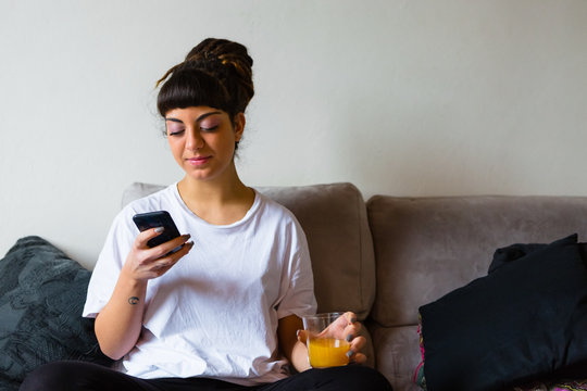 Young Woman with Dreadlocks using a Mobile Phone Sitting on the Sofa