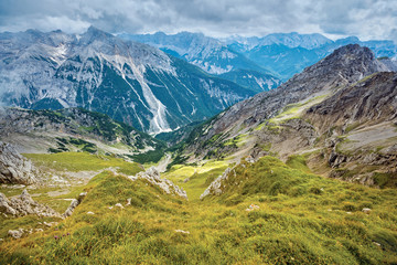 Fototapeta premium Alpine uneven grassy slope under clouds in summer, view downwards