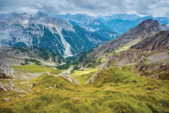 Alpine uneven grassy slope under clouds in summer, view downwards