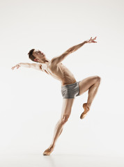 Athletic ballet dancer in a perfect shape performing over the grey background.