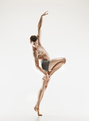 Athletic ballet dancer in a perfect shape performing over the grey background.