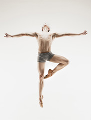 Athletic ballet dancer in a perfect shape performing over the grey background.
