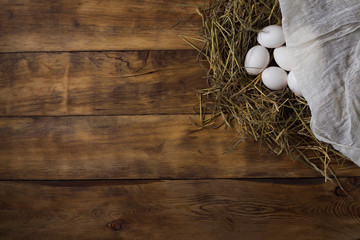 White Chicken Eggs in the Nest and covered with a white cloth on a wooden background. Copy space. Flat lay, top view