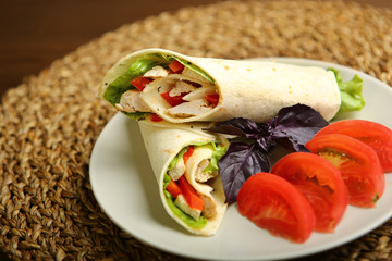 Shaurma without sauce with chicken, pepper, lettuce. Low-calorie roll from pita bread, next to purple basil and slices of tomatoes. Without roasting, raw. Wooden table, wicker stand.