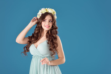 smiling beautiful girl with flowers wreath on head isolated on blue