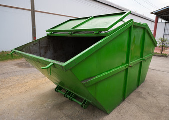 Big green dumpster garbage truck on the road in the factory, Side view