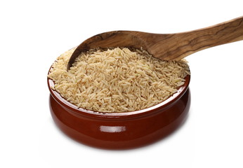 Integral, long grain brown rice pile in porcelain bowl with wooden spoon isolated on white background