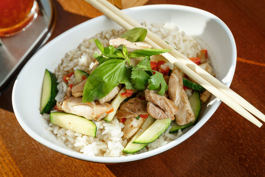 Asian riсe with pork and vegetables in oval plate with bamboo sticks