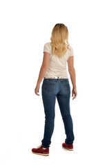 full length portrait of blonde girl wearing simple white shirt and jeans, standing pose, isolated on white studio background.