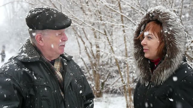 An optimistic view of a wise grey man in a flat cap speaking to his blond daughter in a fur coat. They smile happily in winter in slow motion.